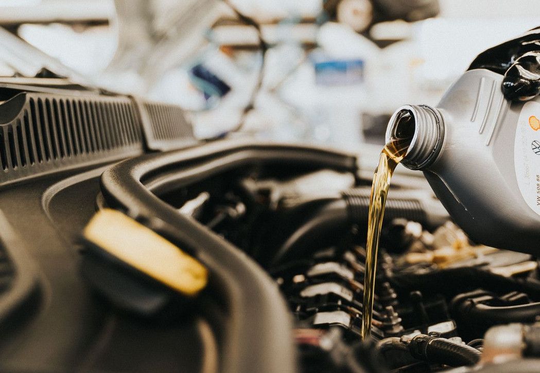 Close-up of a mechanic pouring engine oil into a car engine in an auto repair shop.